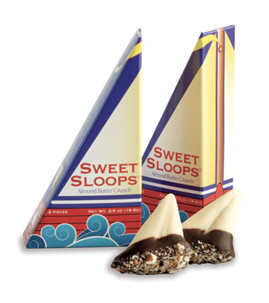 The Sweet Sloops triangular sailboat packaging for Harbor Sweets’ equestrian collection — two sailboat-shaped boxes in red and cream with the Sweet Sloops wordmark, set beside an unwrapped chocolate.