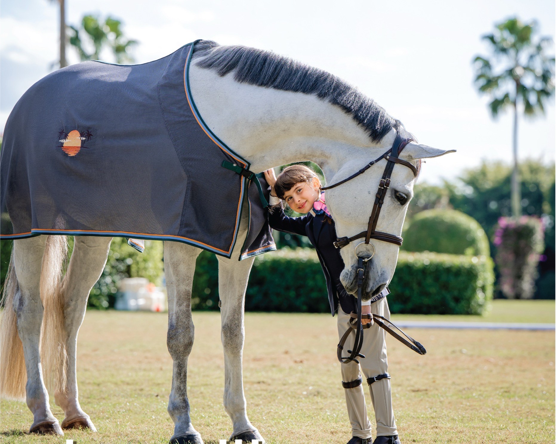 A young rider and a grey horse in a bespoke Clothes Horse blanket, in warm afternoon light.